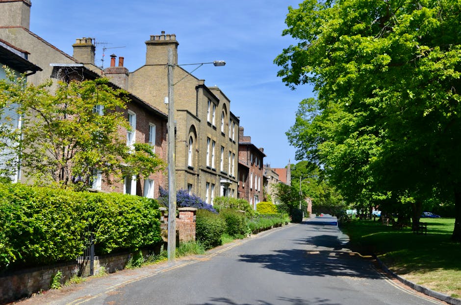 A black and white aerial photograph of a suburban neighbourhood under a partly cloudy sky, with rows of detached and semi-detached houses, each with small gardens and fenced yards, stretching across t